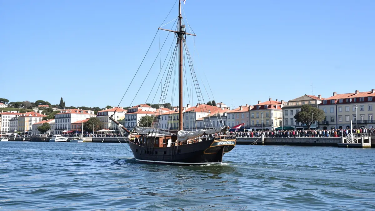A traditional Portuguese bote de fragata sailing on the Tagus River with the Seixal waterfront in the background.