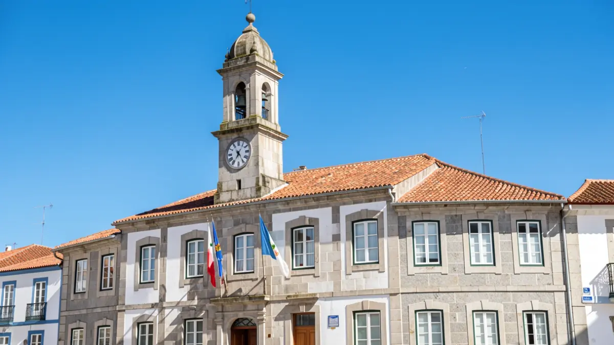 Generic image of a Portuguese town hall building with a clock tower and flags, under a clear blue sky. Traditional architecture with stone facade and tiled roof. Sunny day.