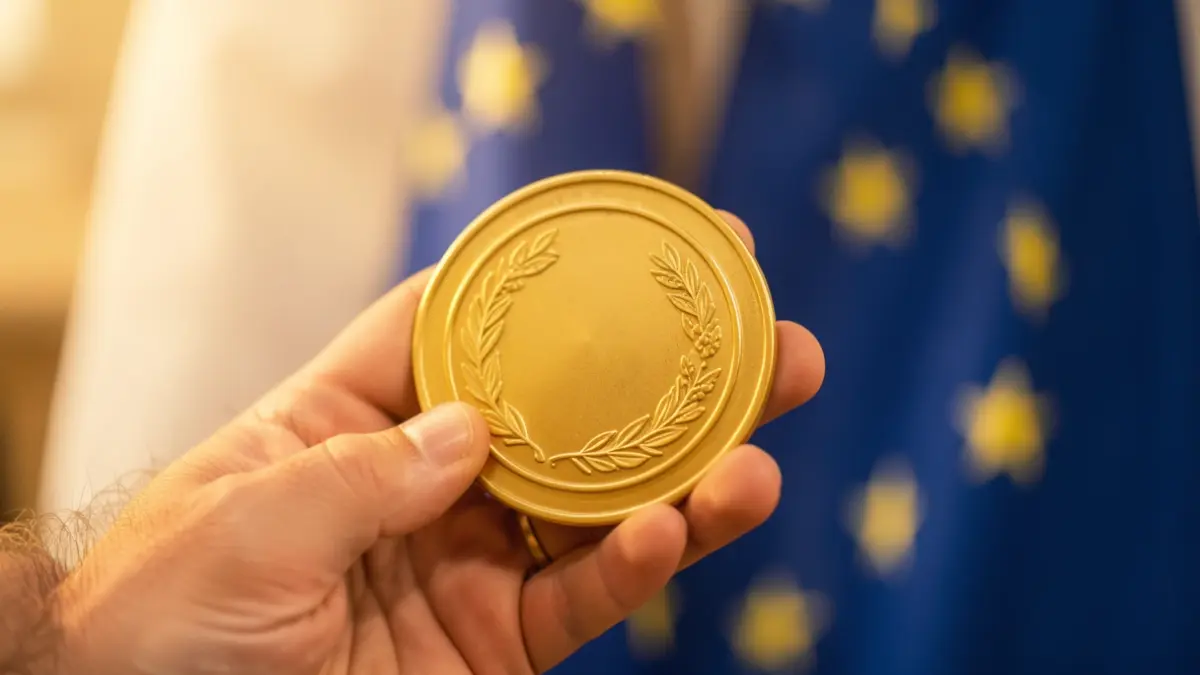 Generic image of a hand holding a golden medal with the EU flag in the background.