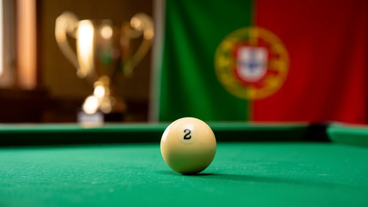 Imagem de uma bola de bilhar sobre a mesa, com um troféu desfocado ao fundo.