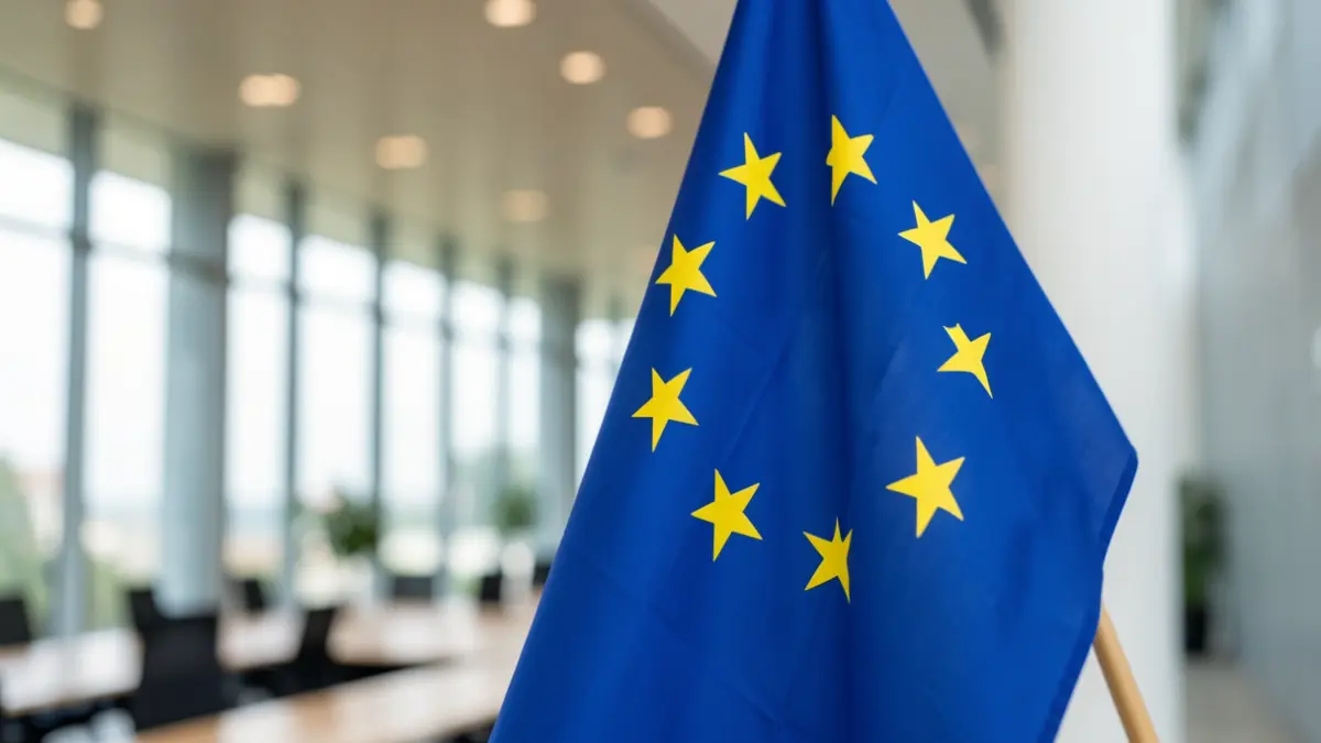 Imagem genérica de uma bandeira da União Europeia em close-up, com um centro de conferências desfocado ao fundo.