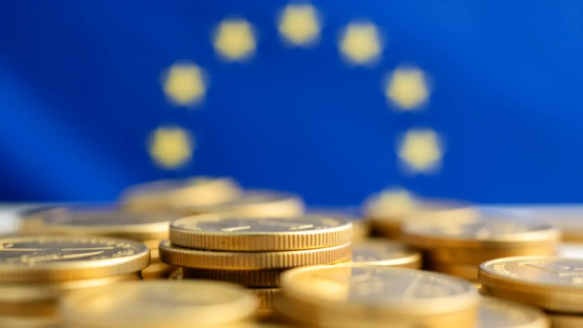 Imagem genérica de fundos de recuperação económica da União Europeia, com moedas douradas desfocadas e um motivo subtil de bandeira da UE ao fundo.