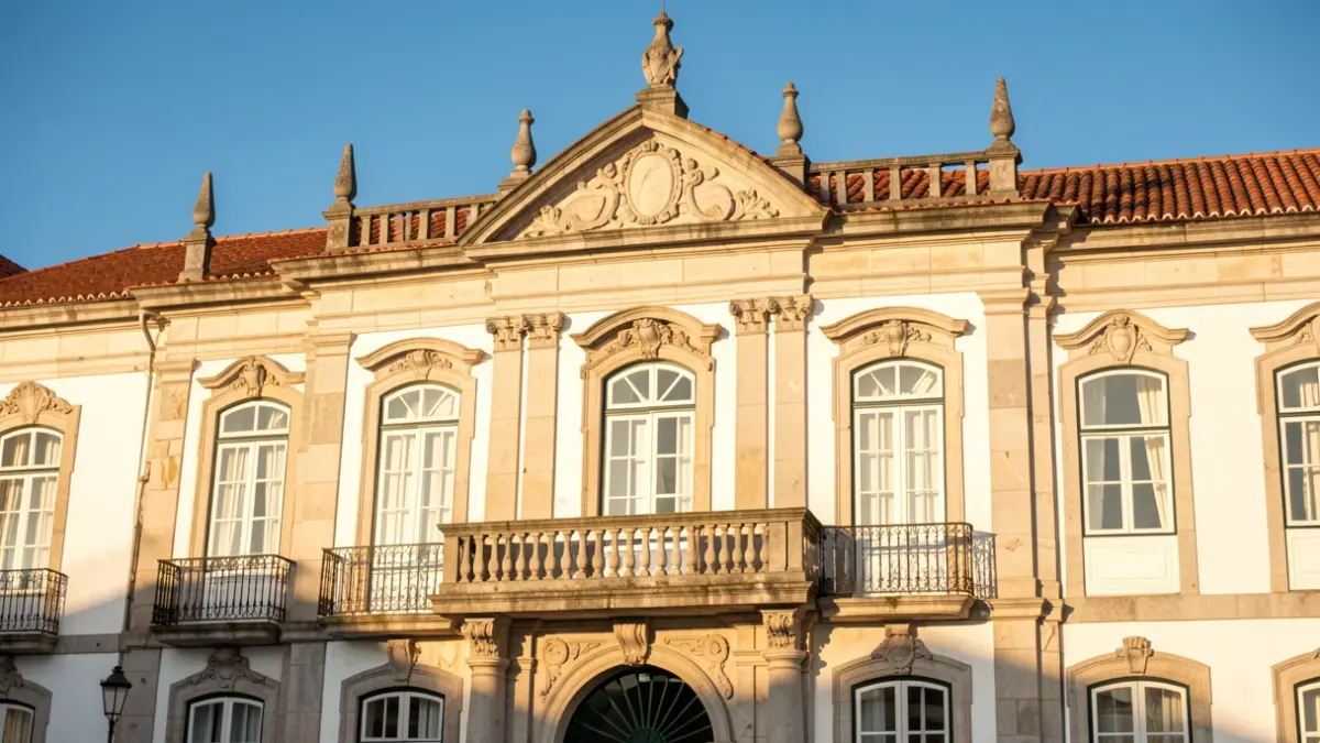 Imagem genérica de uma fachada de edifício camarário português com detalhes em pedra e varanda, sob luz solar de fim de tarde.